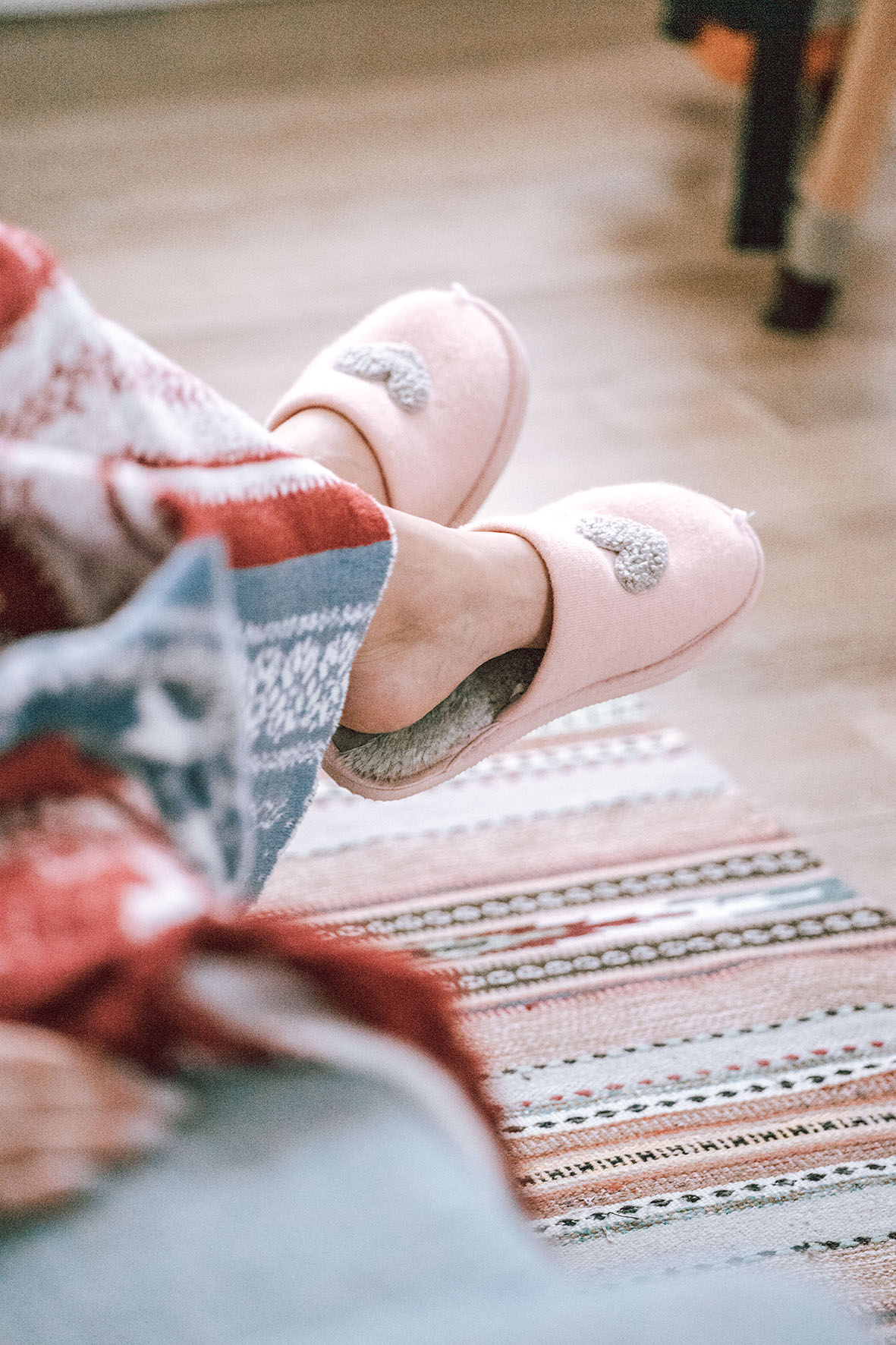 Ett par fötter i mjuka rosa innetofflor och en trasmatta på golvet