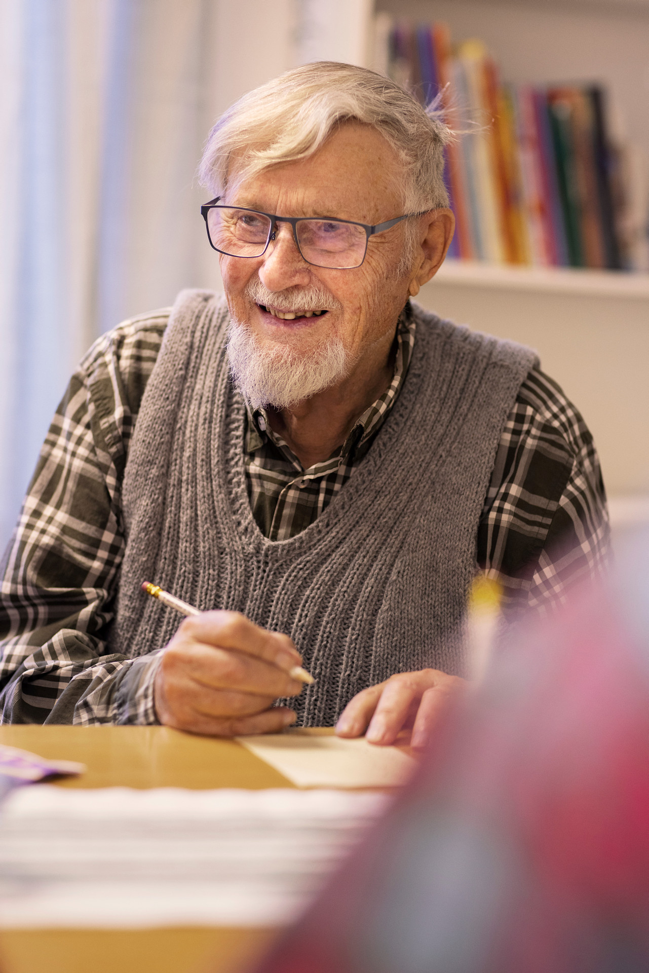 Äldre herre som ser glad ut. Han skriver på ett papper. 
