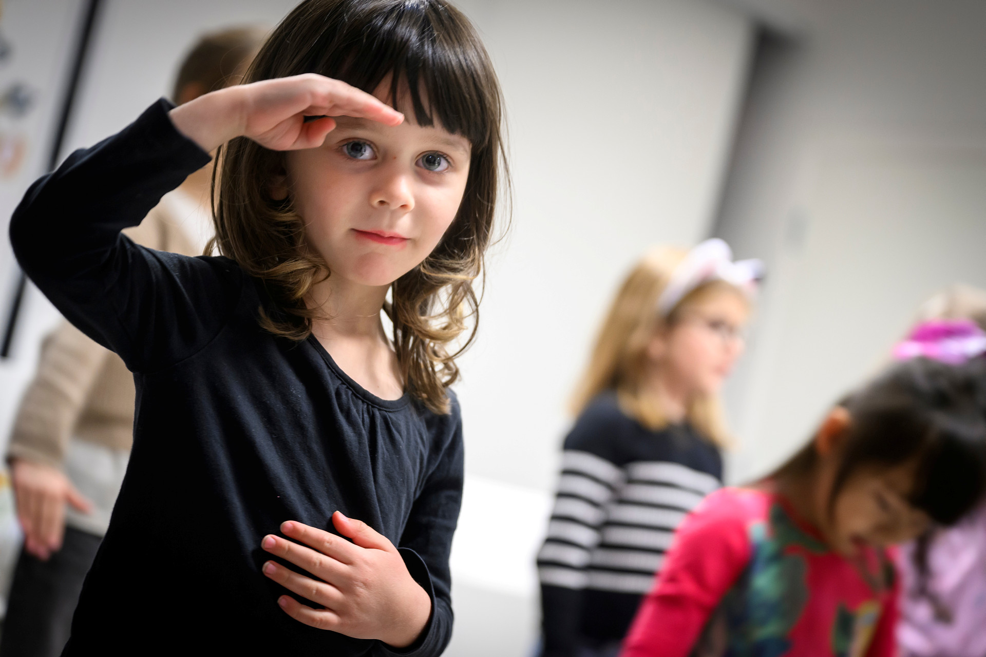 Flicka i svart tröja står tillsammans med andra barn. Hon spejar mot fotografen. 