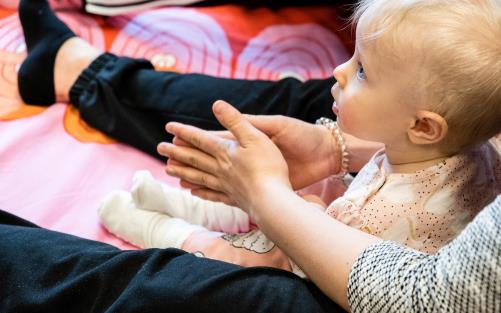 Bebissitter mellan vuxens ben. Vuxen klappar händerna.