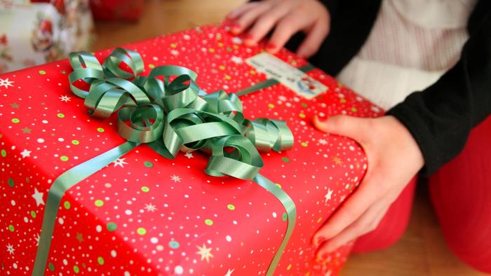 Barnhänder känner på julklapp i rött omslagspapper.