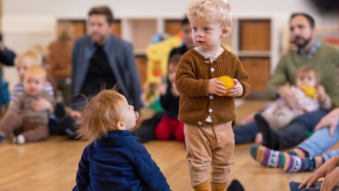 Barn med boll i handen. Runtomkring sitter vuxna och andra barn i en ring.