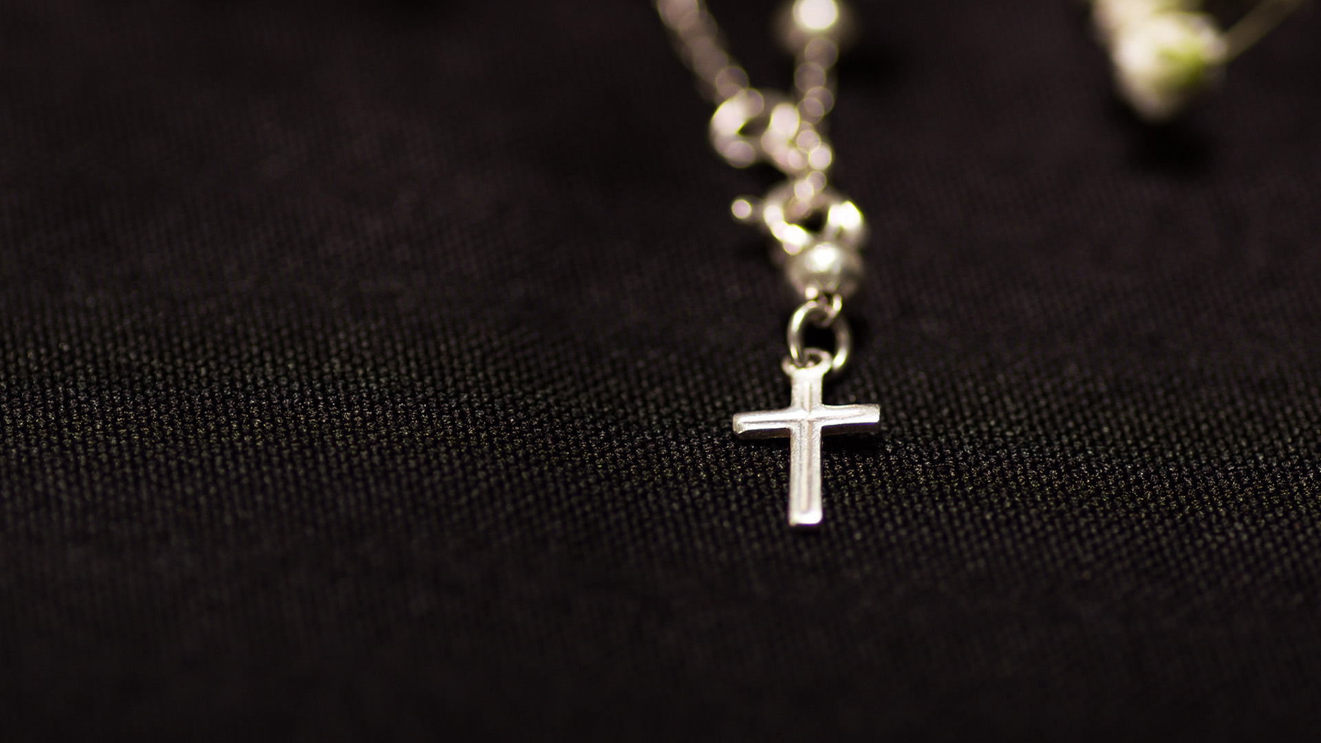 Ett silverkors i ett halsband liggande på en svart bakgrund.