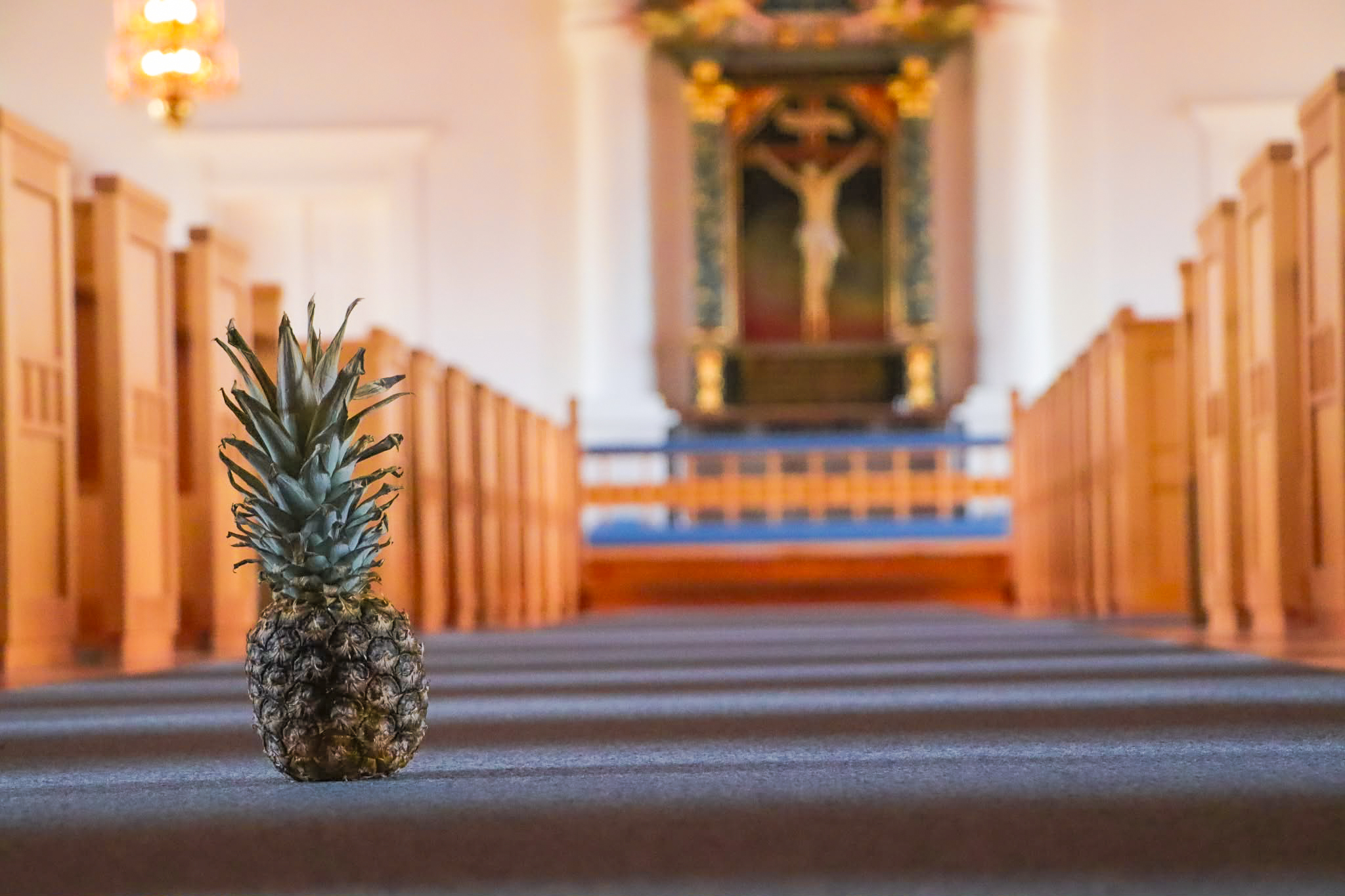 En ananas står på golvet i kyrkan. I bakgrunden syns kyrkbänkar och gången fram till altaret.