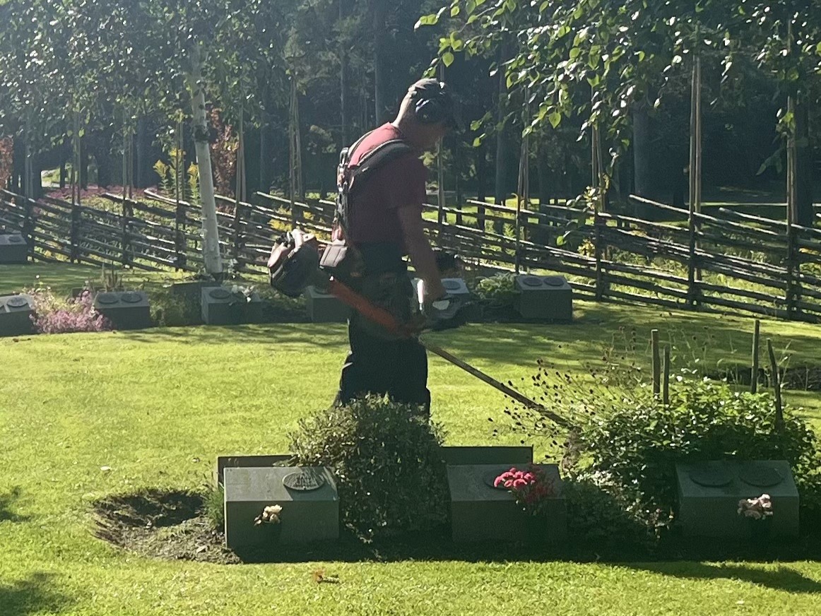 Griftegårdsarbetare trimmar gräs