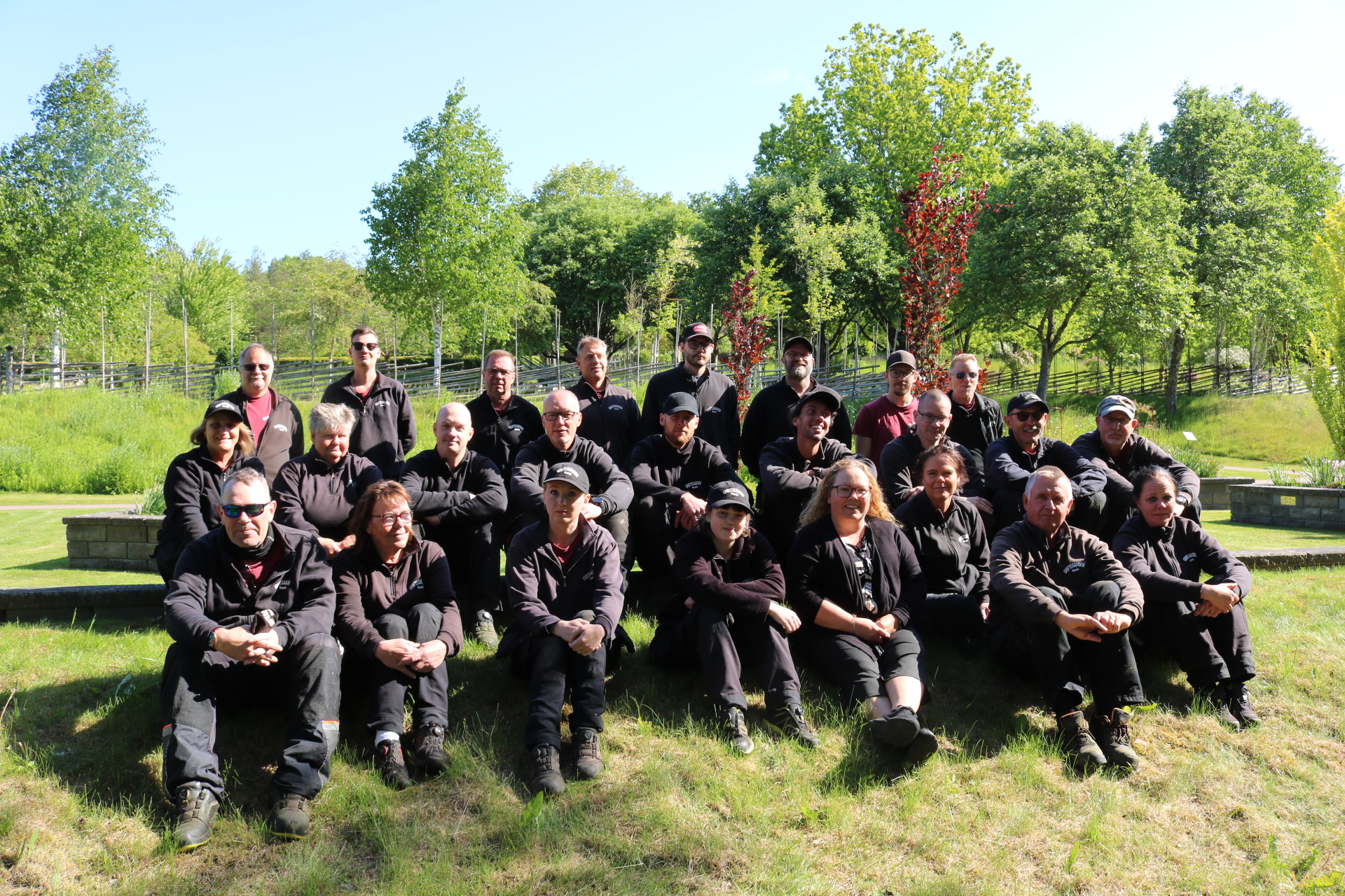 Griftegårdspesonal i svarta kläder sittandes på en gräskulle i solsken.