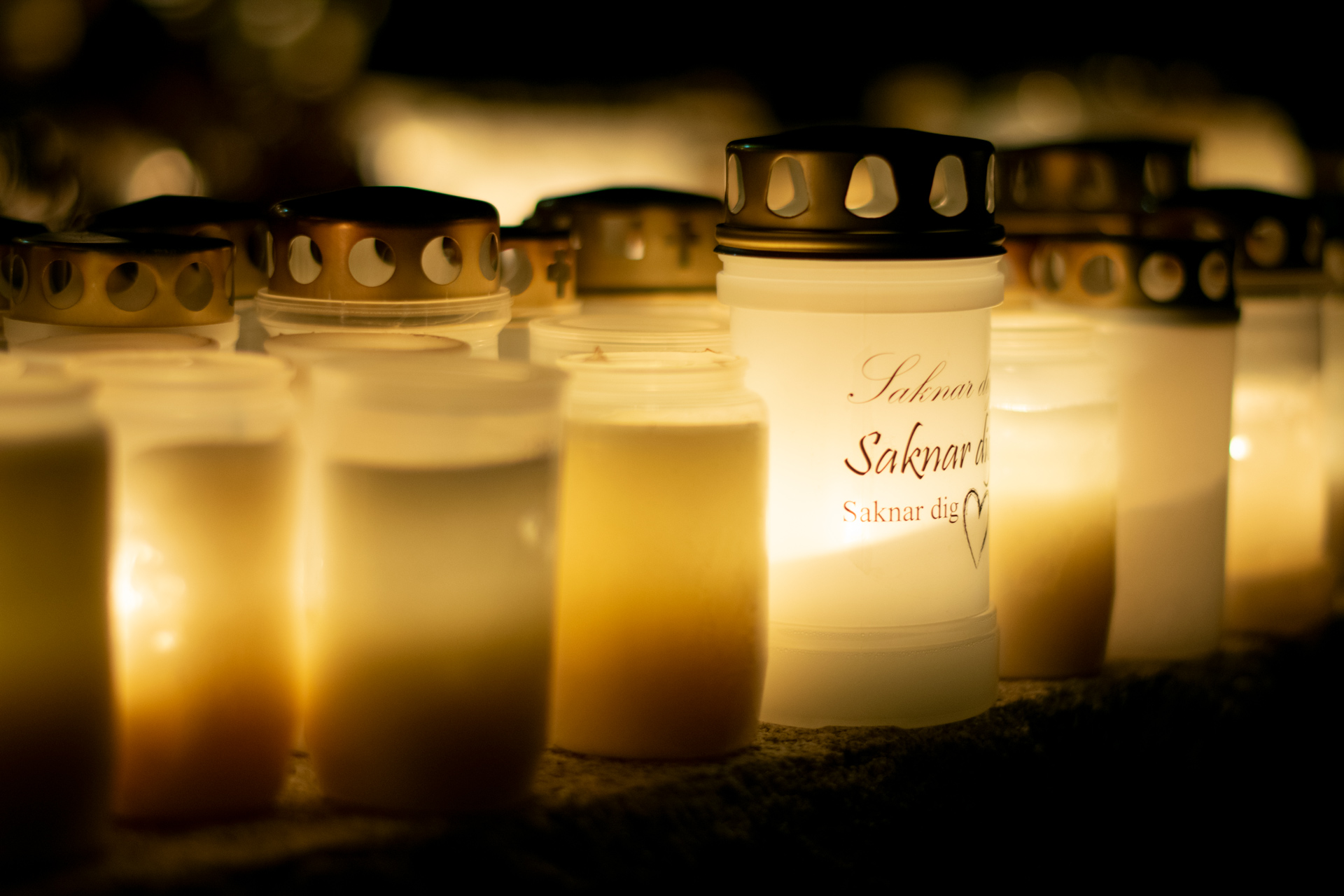 ett tiotal gravljus lyser i mörkret. På ett står texten Jag saknar dig.