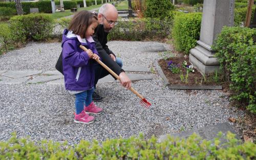En pappa hjälper dotter att kratta gruset på en gravplats med en liten barnkratta.