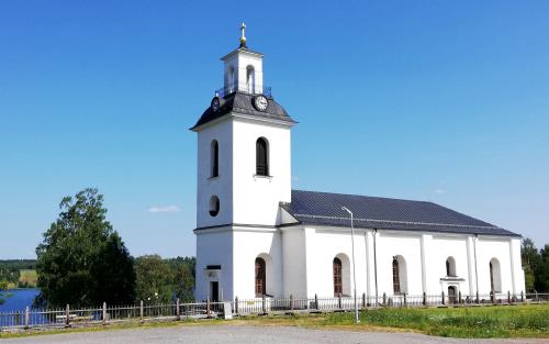 Helgums kyrka. En sommarbild. I bakgrunden skymtar Helgumssjön.