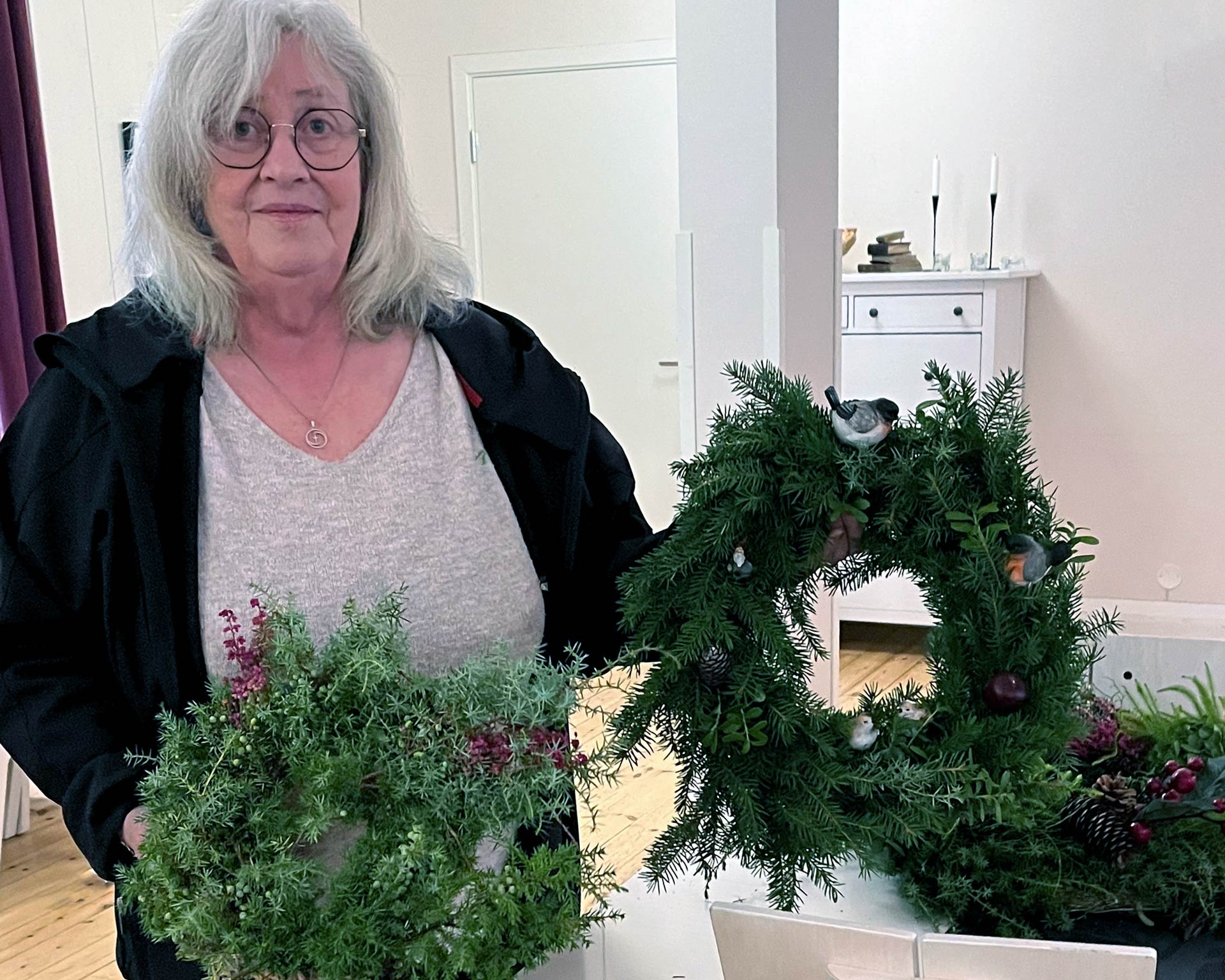 En kvinna håller upp två dörrkransar av en- och granris.