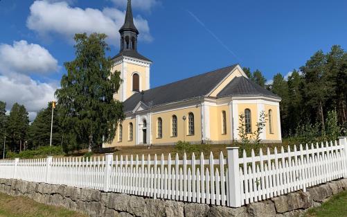 Gulrappad kyrka. I förgrunden ett vitt trästaket.