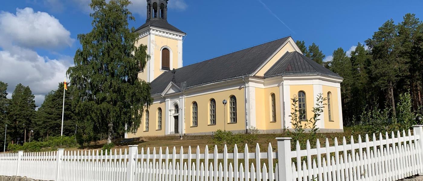 Gulrappad kyrka. I förgrunden ett vitt trästaket.