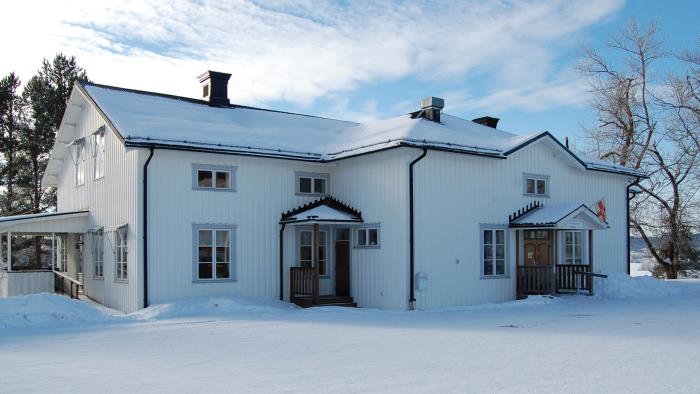 Långsele församlingshem. Vit träbyggnad. En vinterbild. Ovanför entrén hänger Svenska kyrkans flagga.