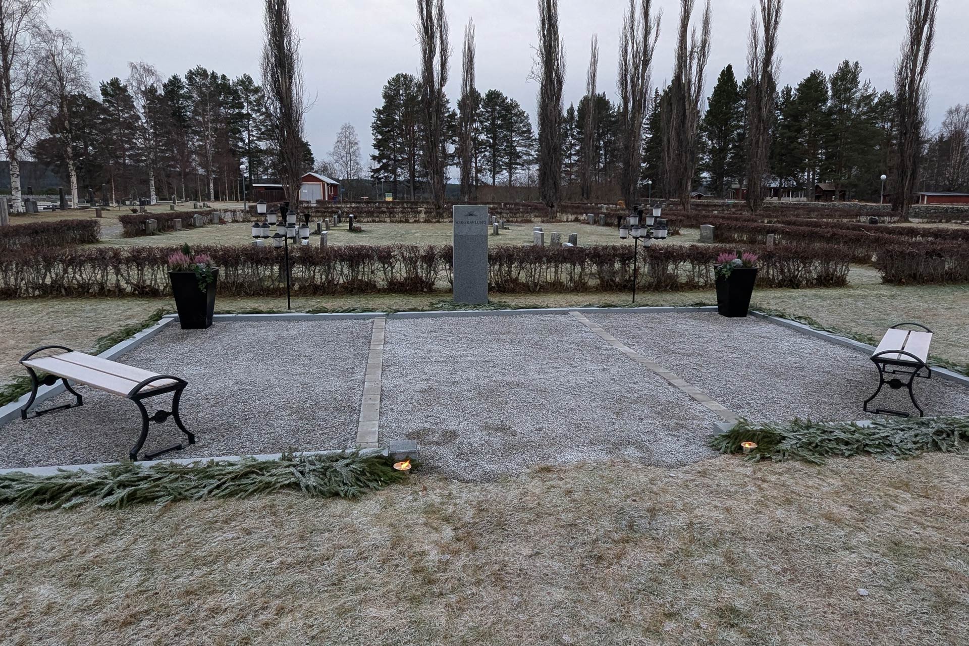 Askgravlund på Junsele kyrkogård. i centrum en sten för plaketter flankerade av två "ljusträd" stora urnor med ljung.