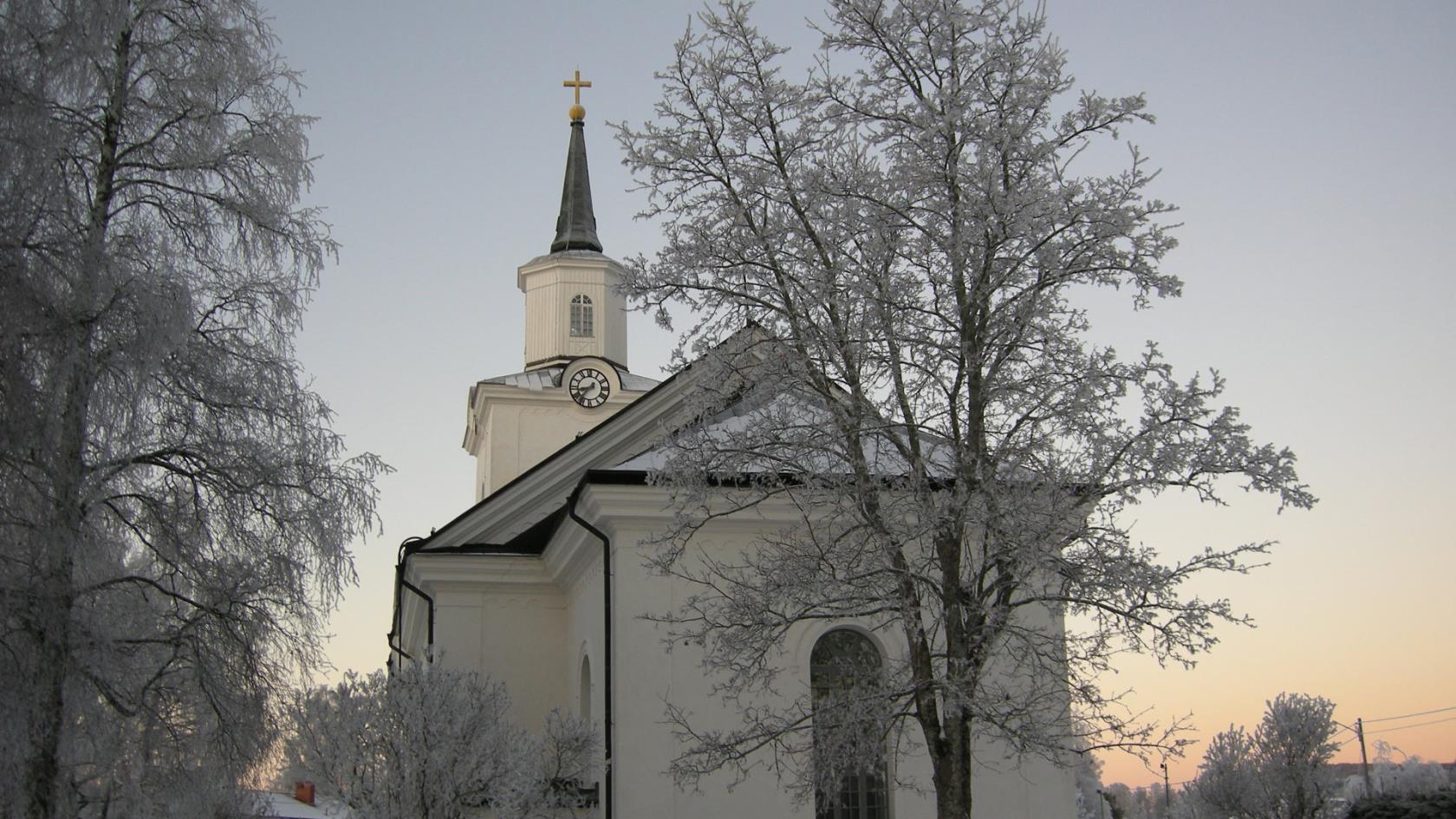 Multrå kyrka i vinterskrud omgiven av frostnupna träd.