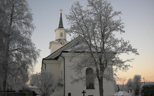 Multrå kyrka i vinterskrud omgiven av frostnupna träd.