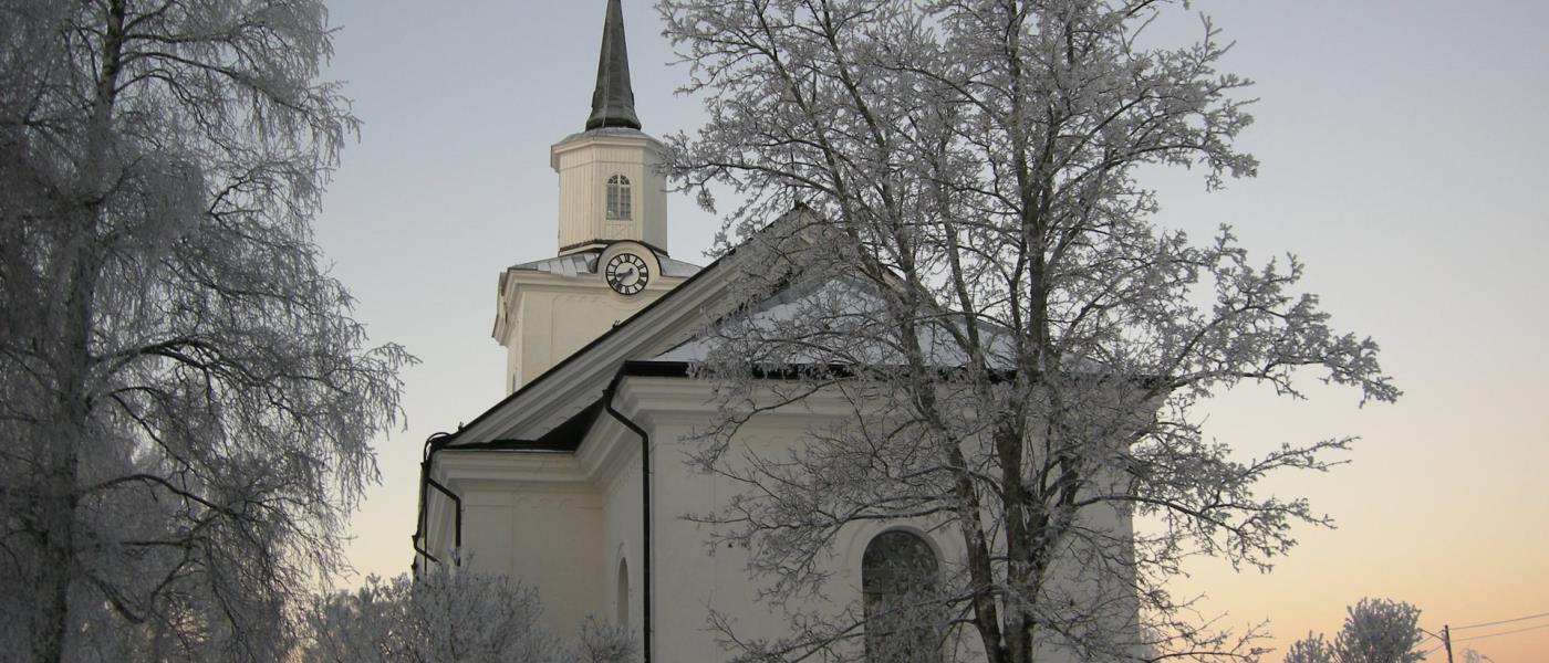 Multrå kyrka i vinterskrud omgiven av frostnupna träd.