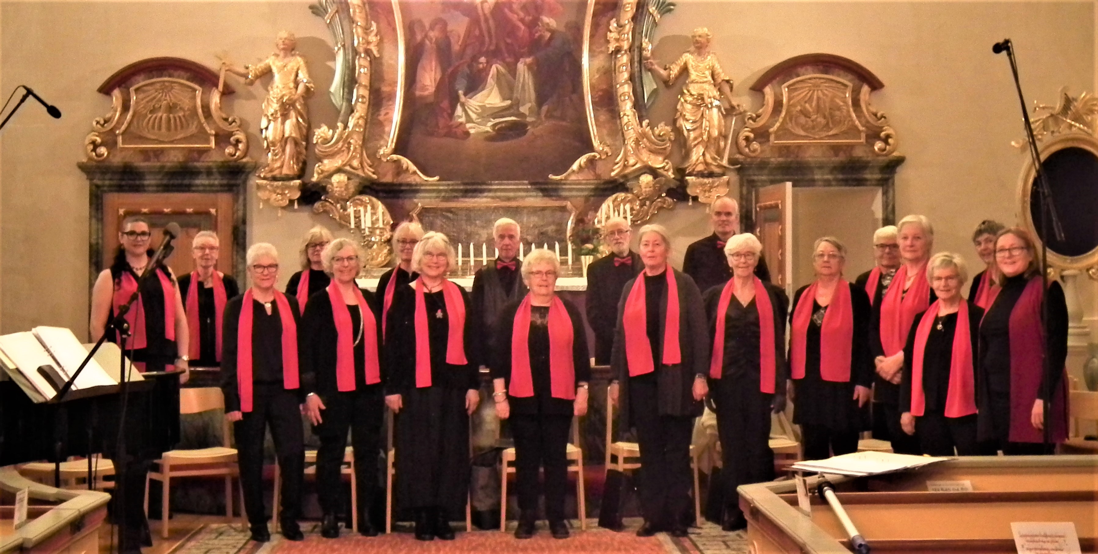 Körmedlemmar uppställda i koret i Multrå kyrka. Samtliga bär svarta kläder. Damerna har röd halsduk och herrarna röd fluga. 