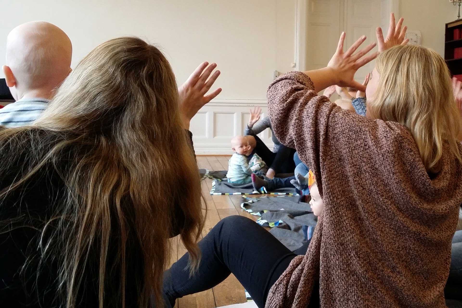 Föräldrar och bebisar sitter på golvet och sjunger.