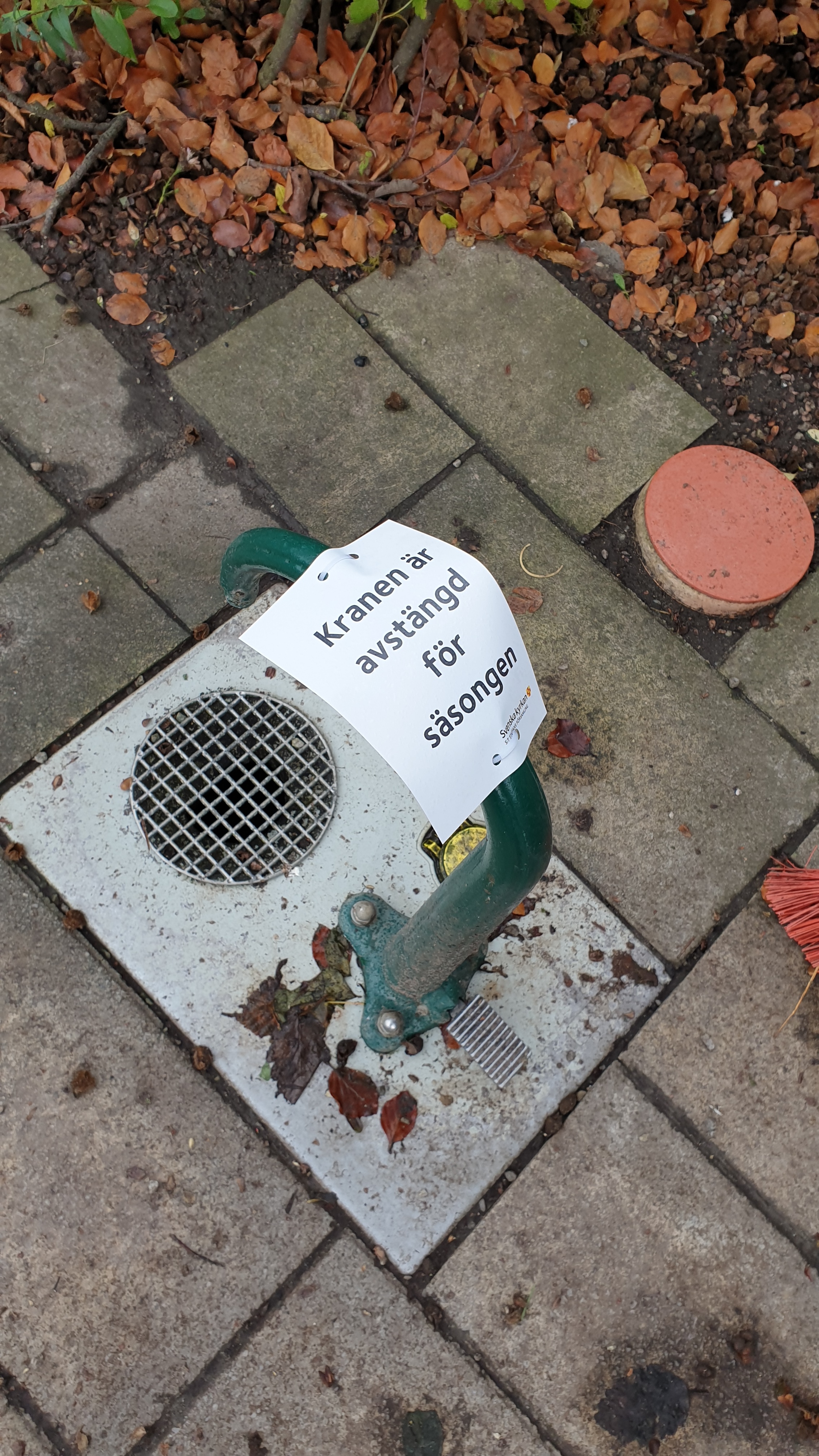 Vattenkran på kyrkogård, med skylt om stängning för säsongen.