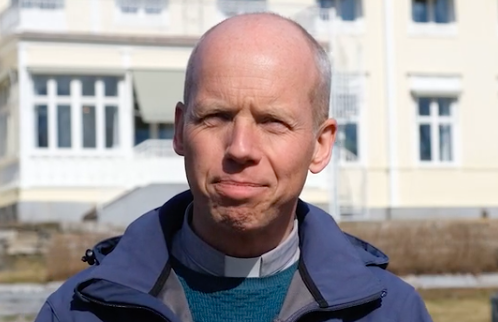 Prästen Johan Holmgren i blå jacka och med prästskjorta står framför Prästgården i Skellefteå, en gul byggnad med anor.