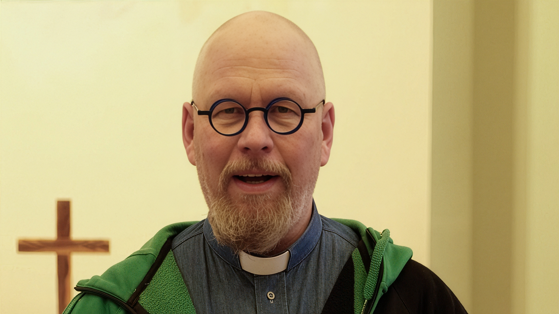 Bilden visar prästen Anders Hedström. Han har runda glasögon med mörkblå bågar och en prästskjorta i jeanstyg.