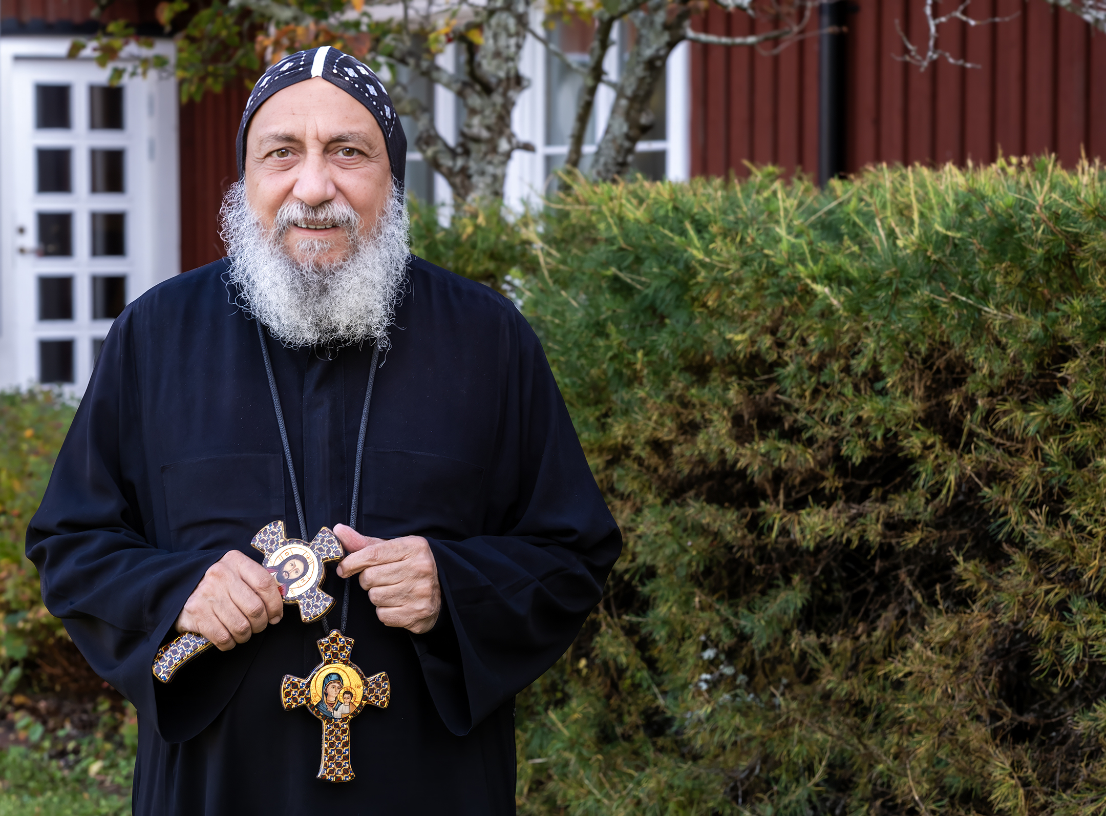 Bilden föreställer Biskop Thomas, biskop i koptiska kyrkan. Han har en svart kaftan och det hänger ett stort träkors i ett band runt halsen. Han har ett stort grått skägg och en hätta på huvudet.