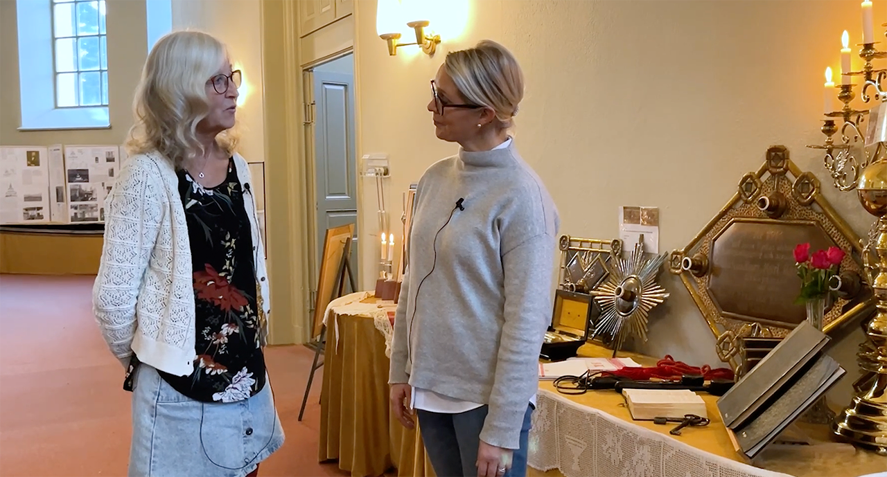 Christina Ershag (t.v.) och Gabriella Fahlman Andreasen (t.h.)  står framför den utställning som skapats i samband med Byske kyrkas 150-årsjubileum, oktober 2022.