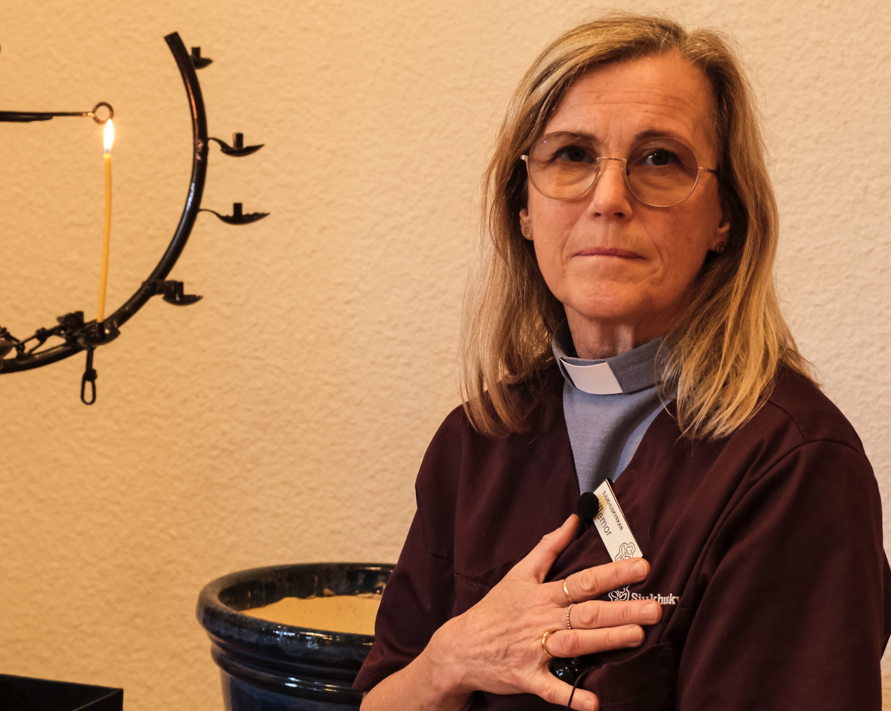 Sjukhuspastorn Lillemor Ivansson i sjukhuskläder vid en ljusbärare med handen på hjärtat