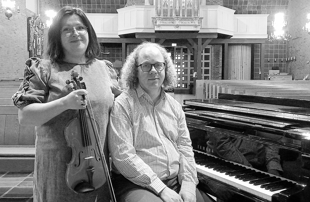 Musikerna Maria Sjöstedt, violin, och Lars Sjöstedt, piano står i en kyrka vid en flygel. Maria håller violinen i sin hand och Lars sitter vid flygeln. 