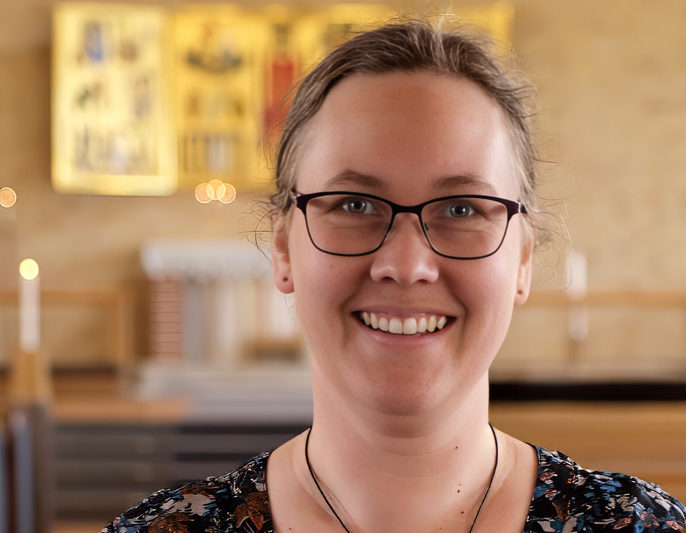 Bilden föreställer Marta Eriksson ståendes framför guldskimrande altartavla i S:t Mikaels kyrka i Jörn