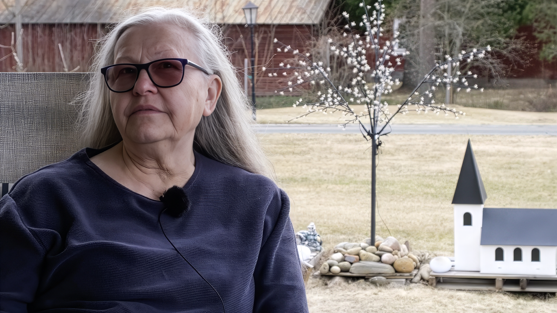 Bilden föreställer Rosalie Keller, en kyrkvärd och förtroendevald. Hon har mörka glasögon och grått långt hår. Hon sitter ute på altanen och har en gräsmatta och ett ljusträd i bakgrunden.