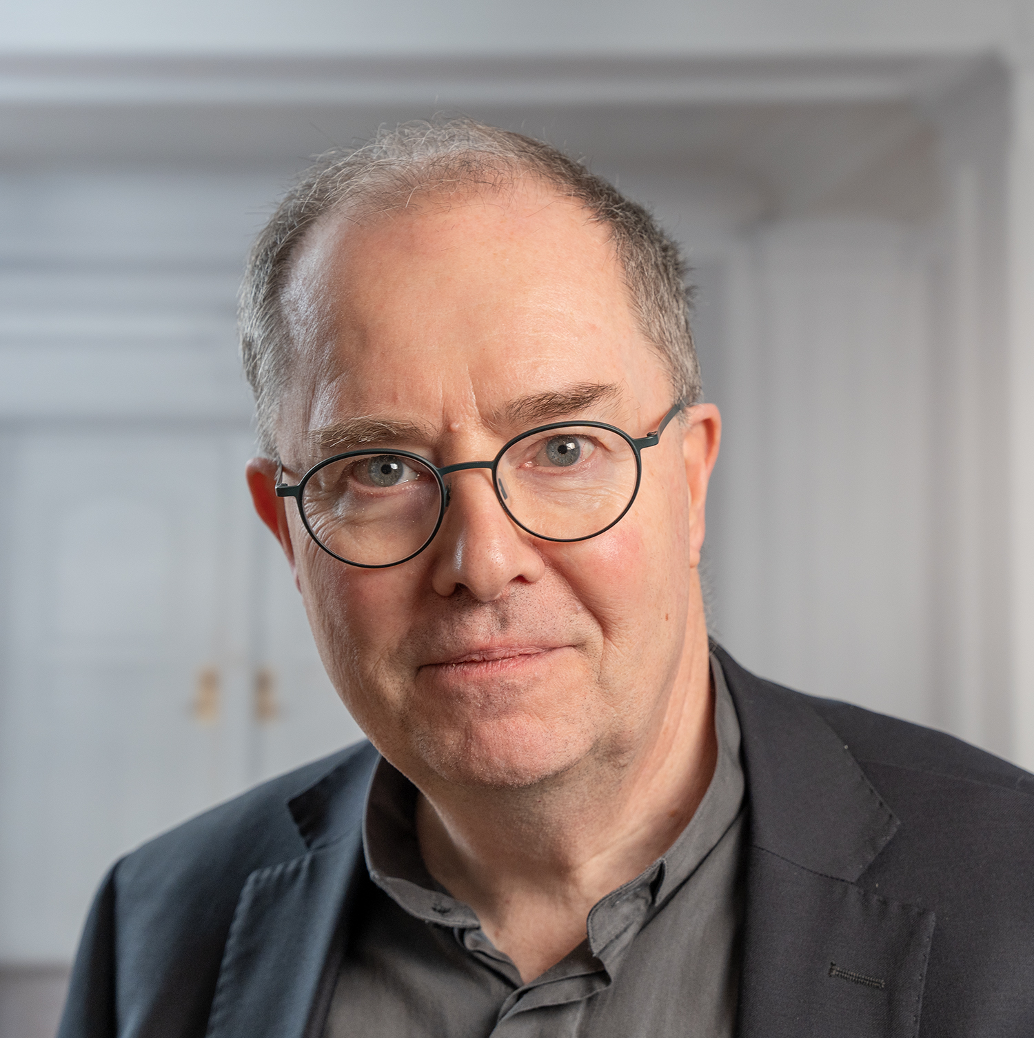 Bilden visar Pater Ulf Jonsson i porträttläge. Han bär en grå skjorta, svart kavaj och glasögon.