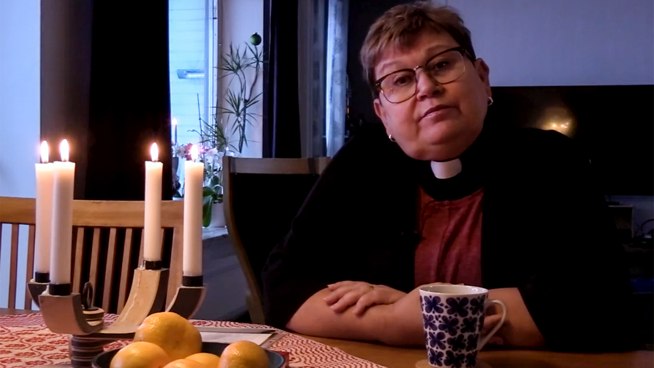 Kyrkoherde Ulrika Markgren sitter vid sitt köksbord och 4 ljus är tända i adventsstaken. 