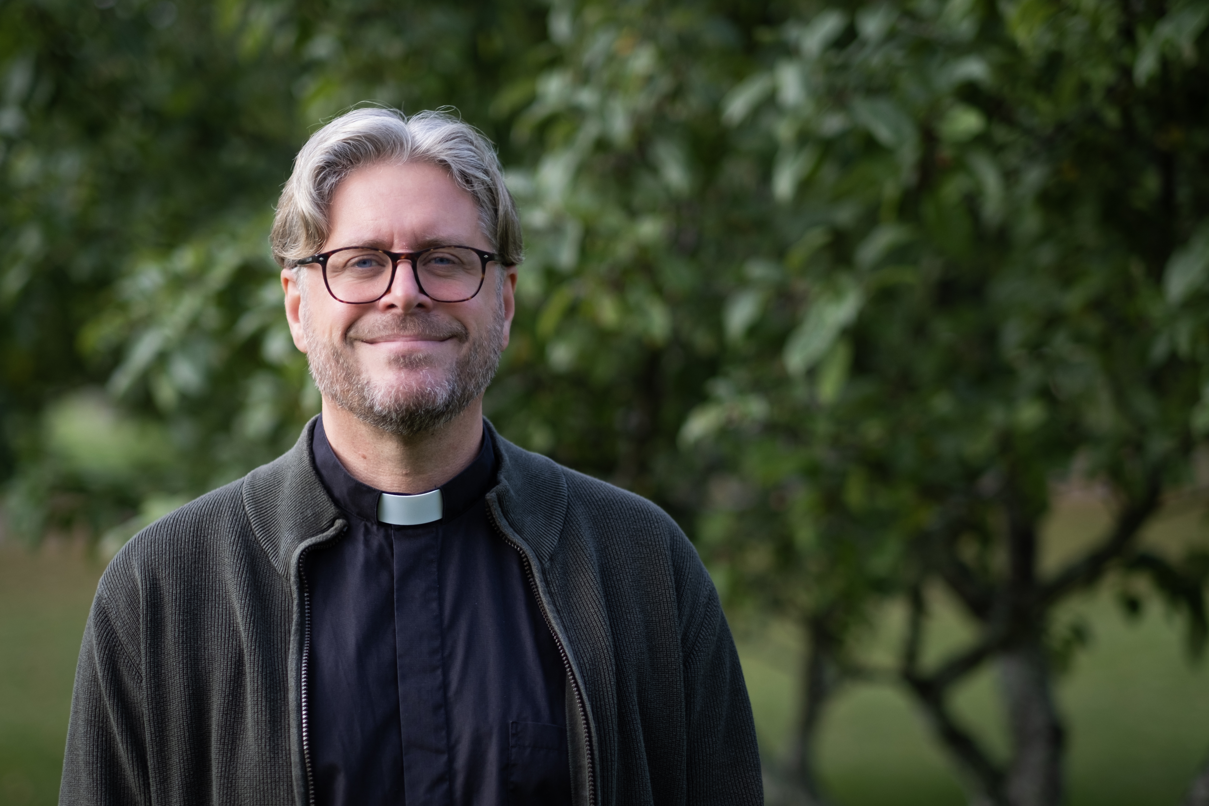 Prästen Dan Richardsson, iklädd svart prästskjorta, grön bakgrund