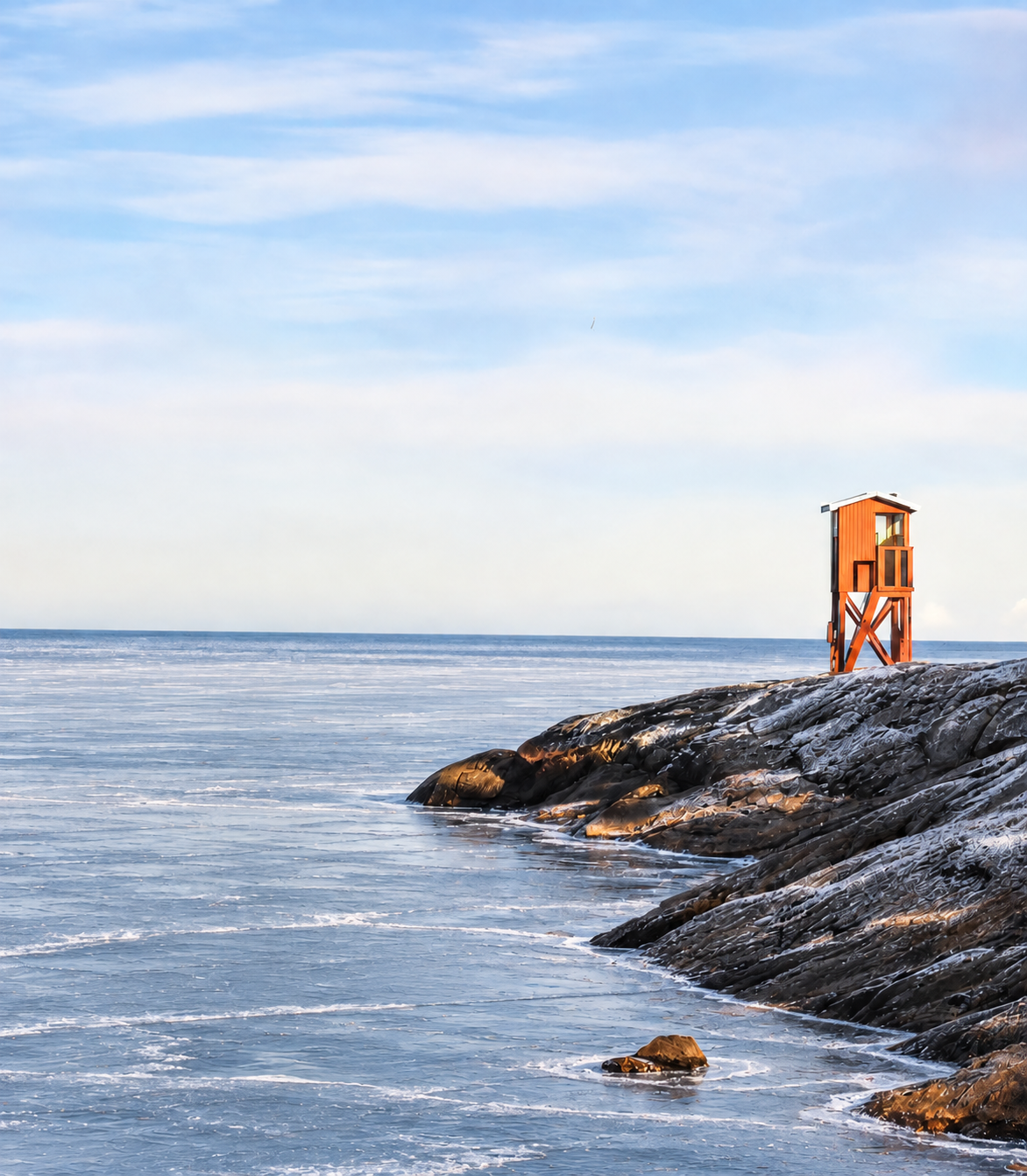 Bild på klippor och ett utsiktstorn. På havet ligger ett tunt istäcke