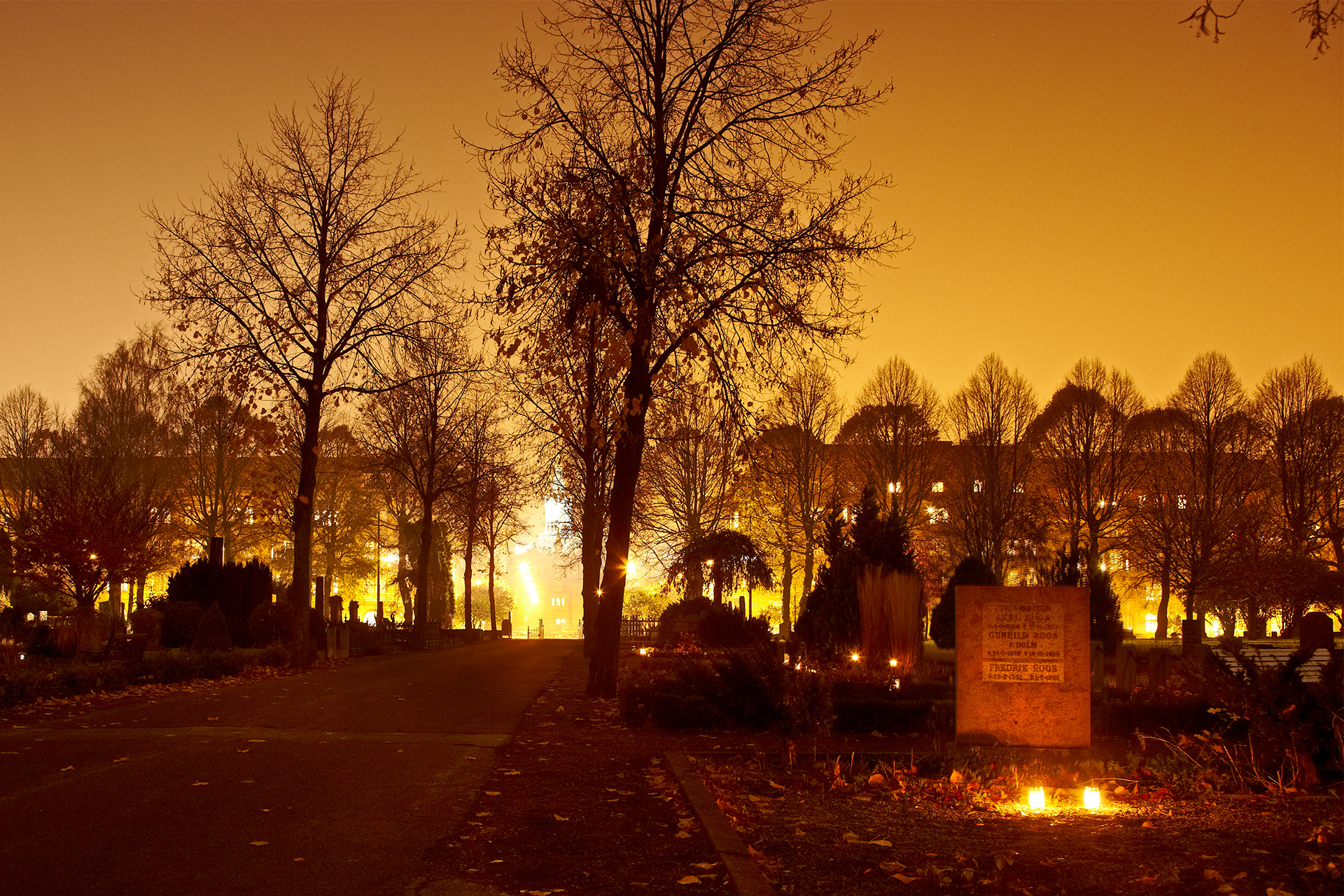 Kväll på kyrkogård med gravsten i förgrunden mot gulaktigt himmel.