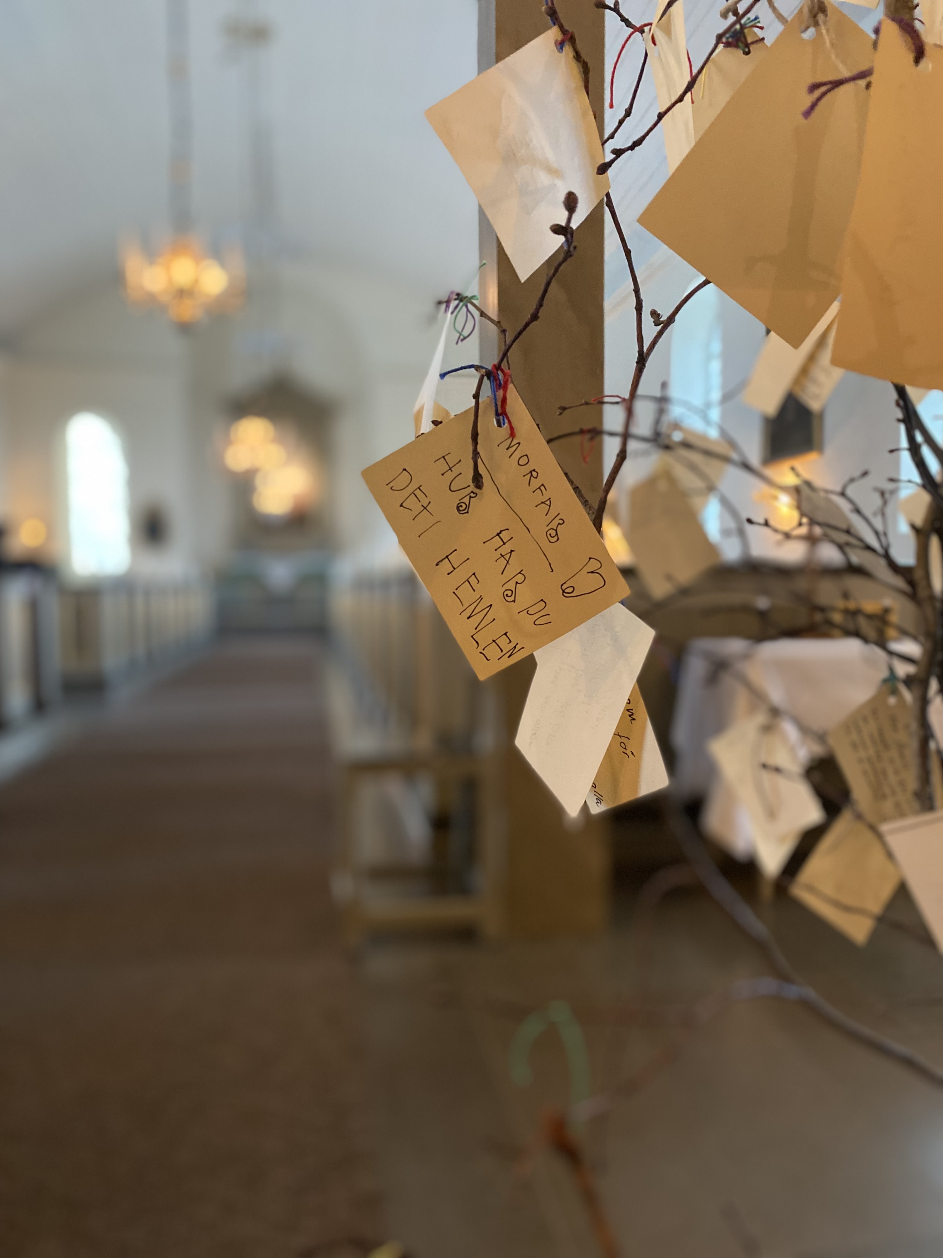 Bönelappar hänger i en krist i kyrkan. "Hej morfar, hur har du det i himlen?" står med ett barns handstil på en av lapparna.