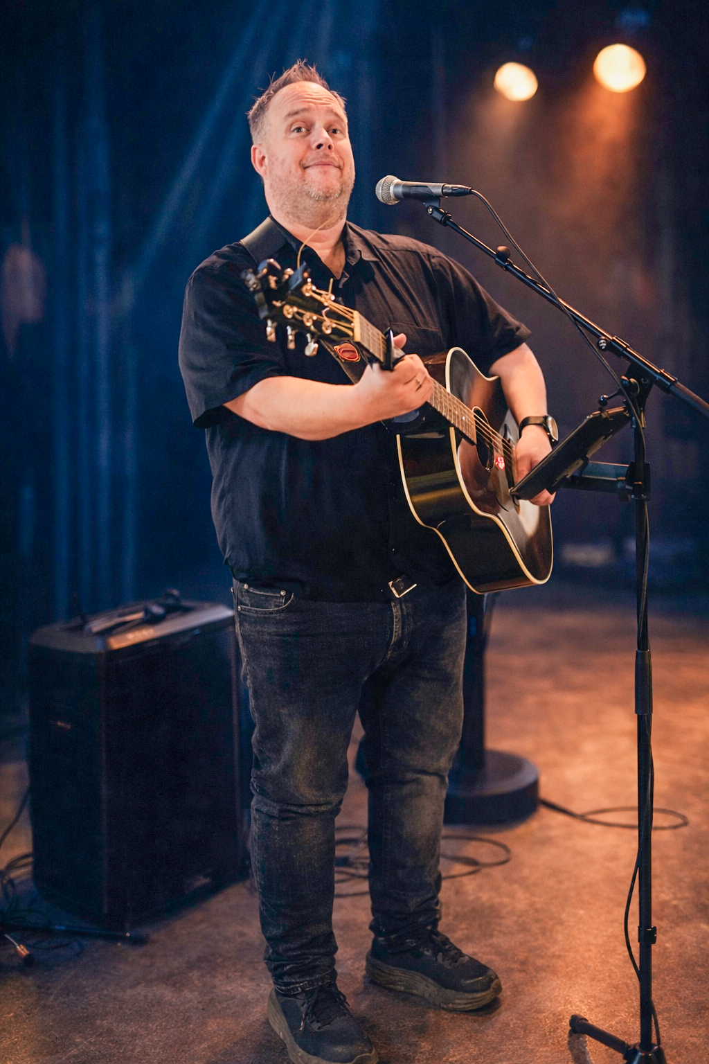 En blond man med gitarr står på en scen.