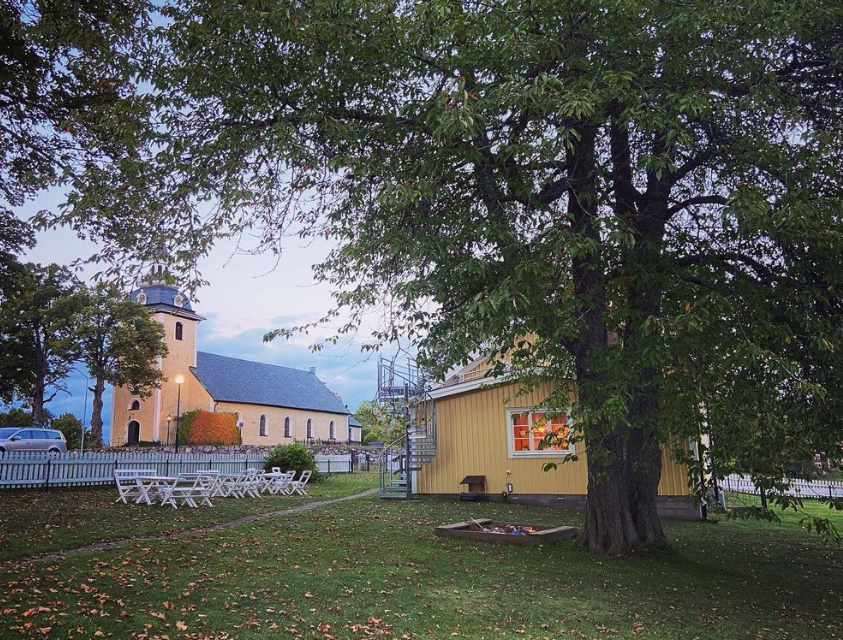 Snavlunda kyrka och församlingsgård omgiven av träd, höstlöv på marken