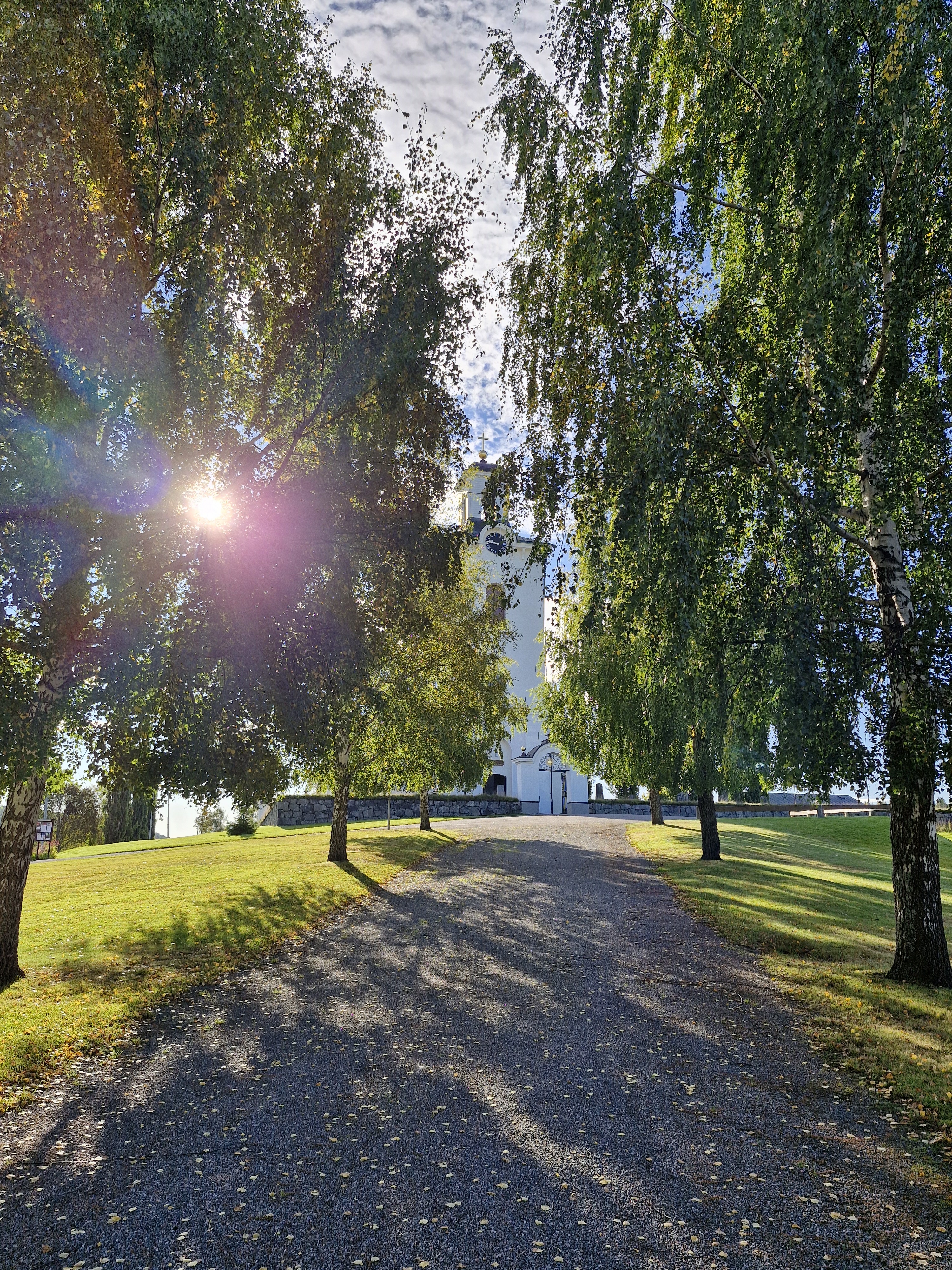 Solen faller genom träden framför Nätra kyrka.
