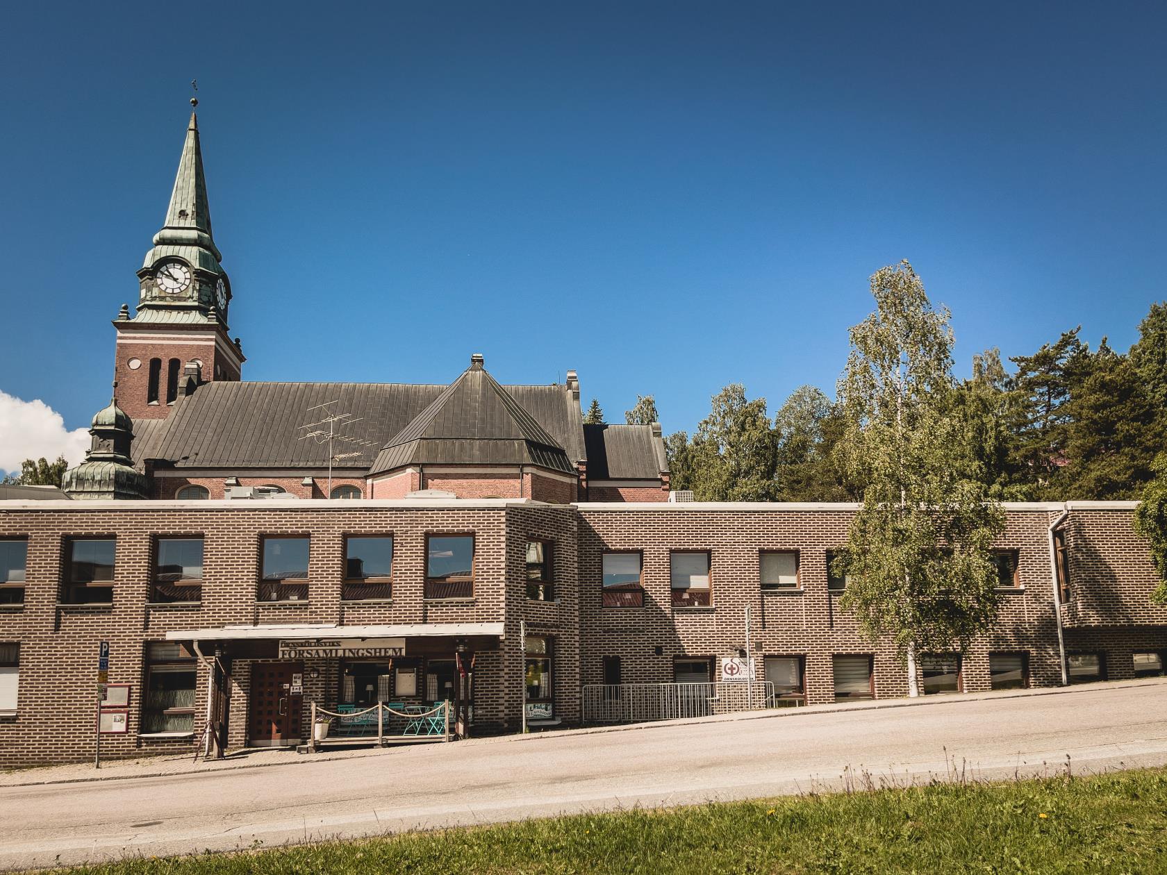 Tegelbyggnad med många fönster och en kyrka i bakgrunden