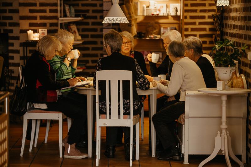 En grupp människor runt ett bord som sitter och pratar och fikar.