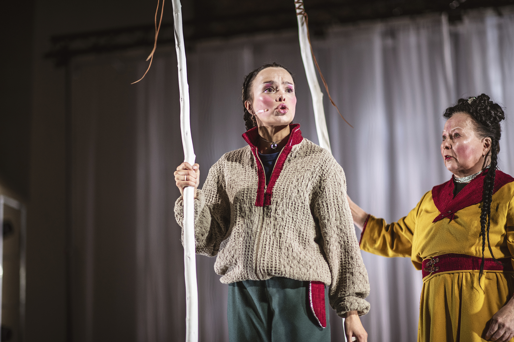 Två kvinnor klädda i samiska kläder, som håller i var sin stav.