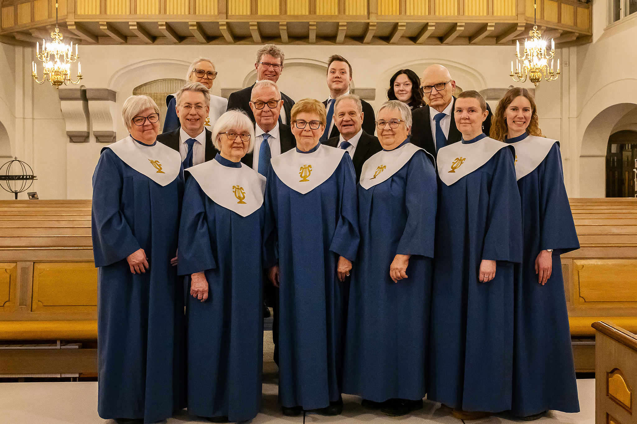 En grupp kvinnor och män uppställda i en kyrkan där kvinnorna är klädda i kåpor och männen i kostym.
