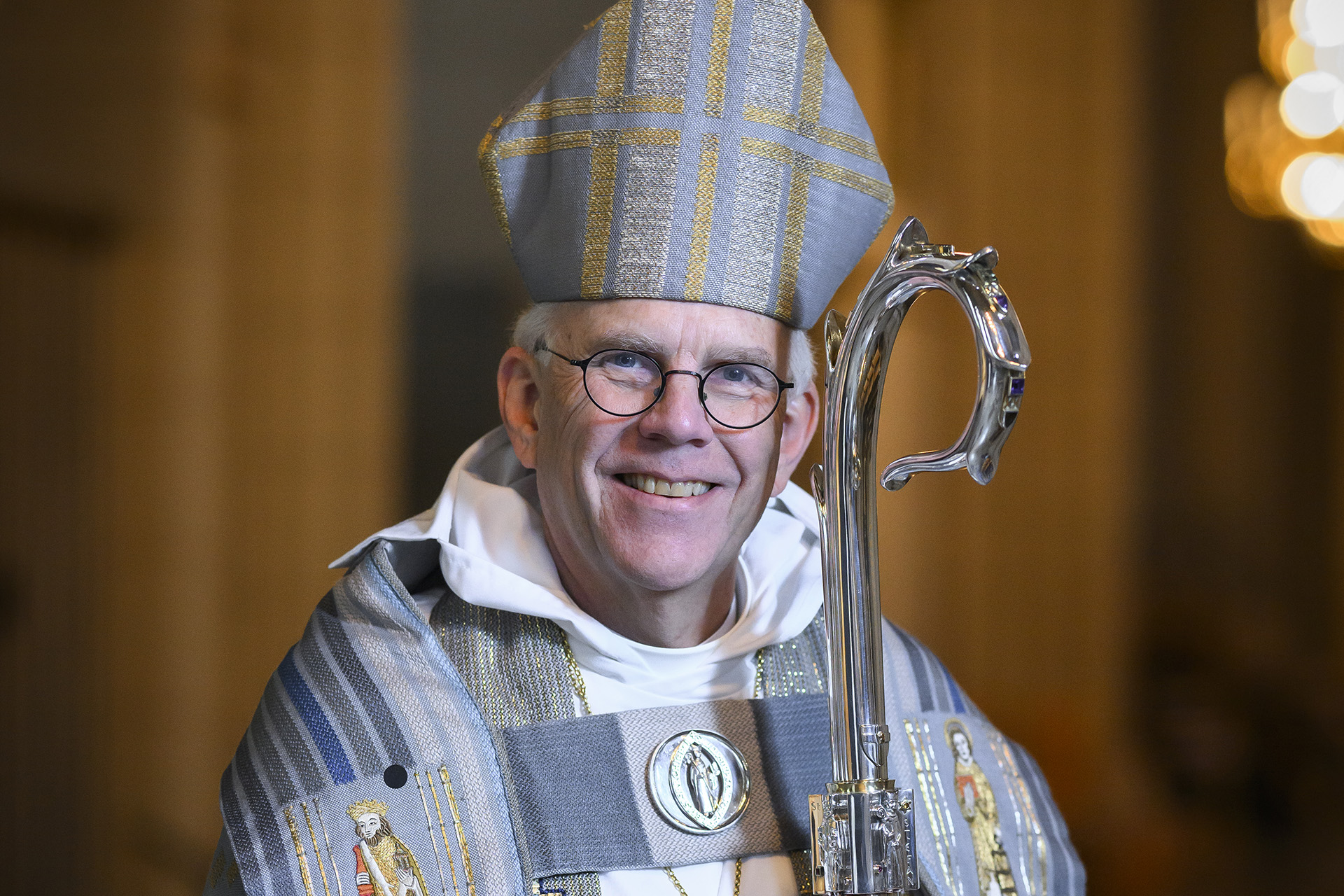 Ärkebiskop Martin Modéus fotograferad i Uppsala domkyrka, leende och i fullornat med kräkla och mitra i silver och ljusblått.