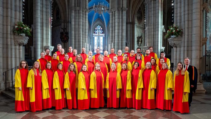 Kammarkören Collegium Cantorum står uppställda i sina rödgula kåpor i domkyrkans korsmitt, med Kristallkorset i bakgrunden.