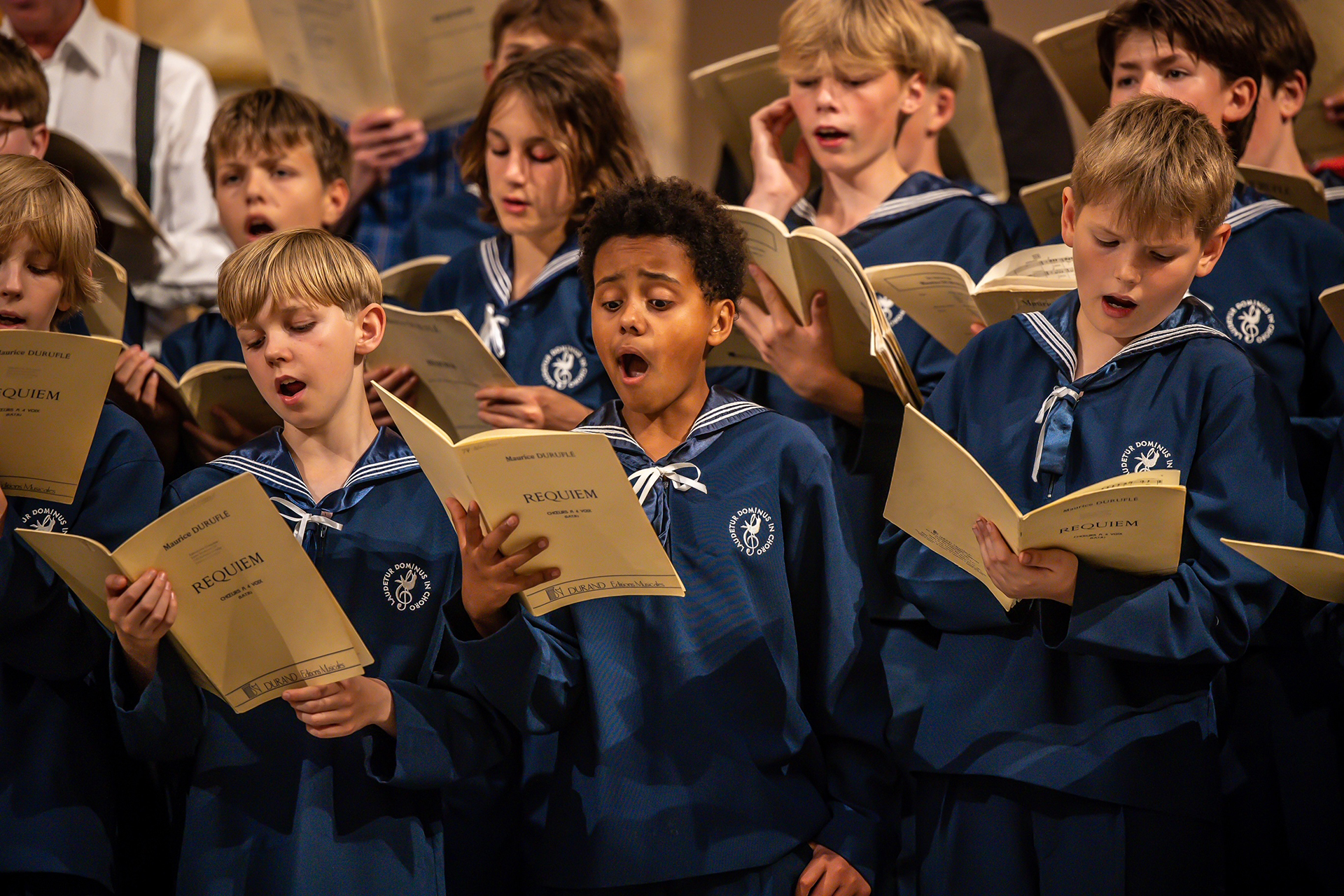 Gosskörsångare i lägre skolåldern sjunger i blå sjömansskjortor och med noter i hand.