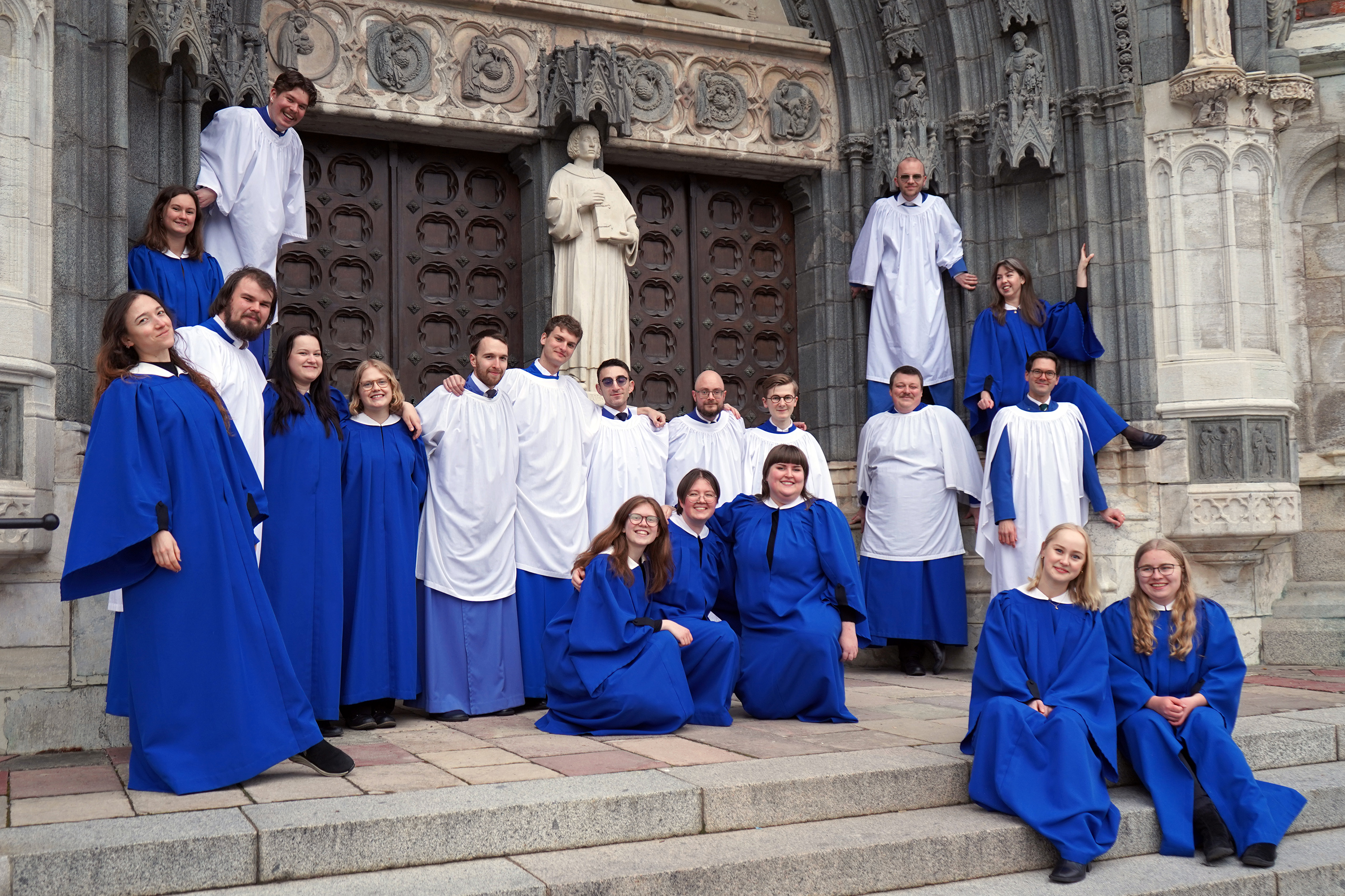 Schola Cantorum spexar iförda blå och vita kåpor utanför södra porten vid Uppsala domkyrka.