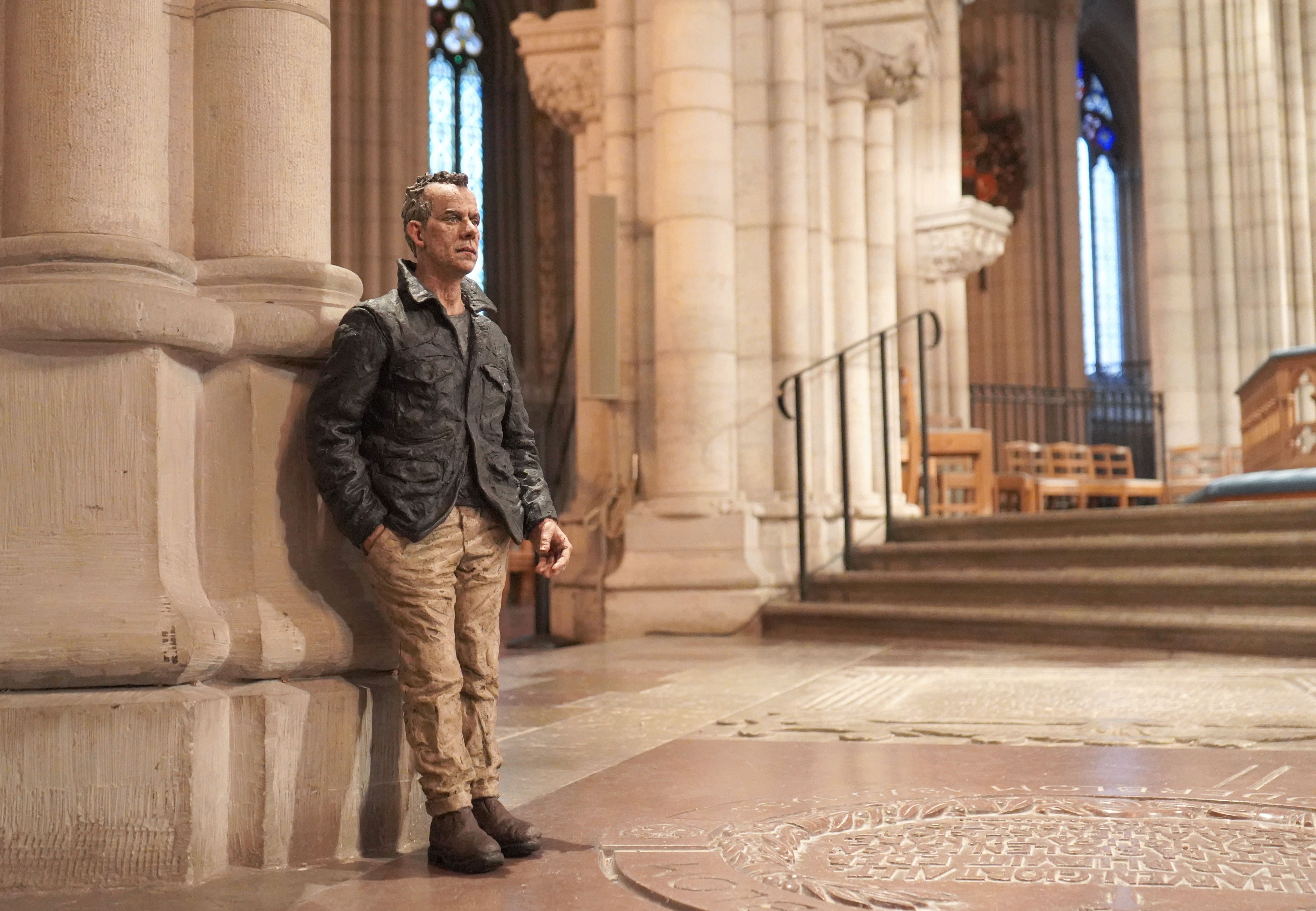 En skulptur i form av en man med skrynkliga former står lutad mot en pelare i domkyrkans högkor.